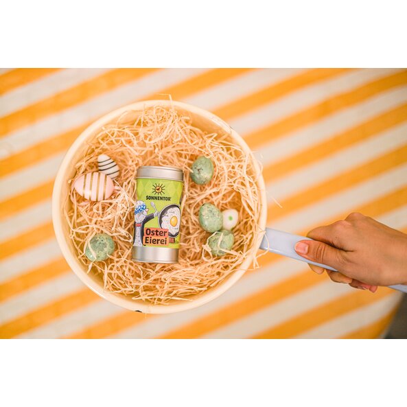 Foto mit Oster Eierei Streudose in Pfanne mit Ostereier und gelb weißem Hintergrund.